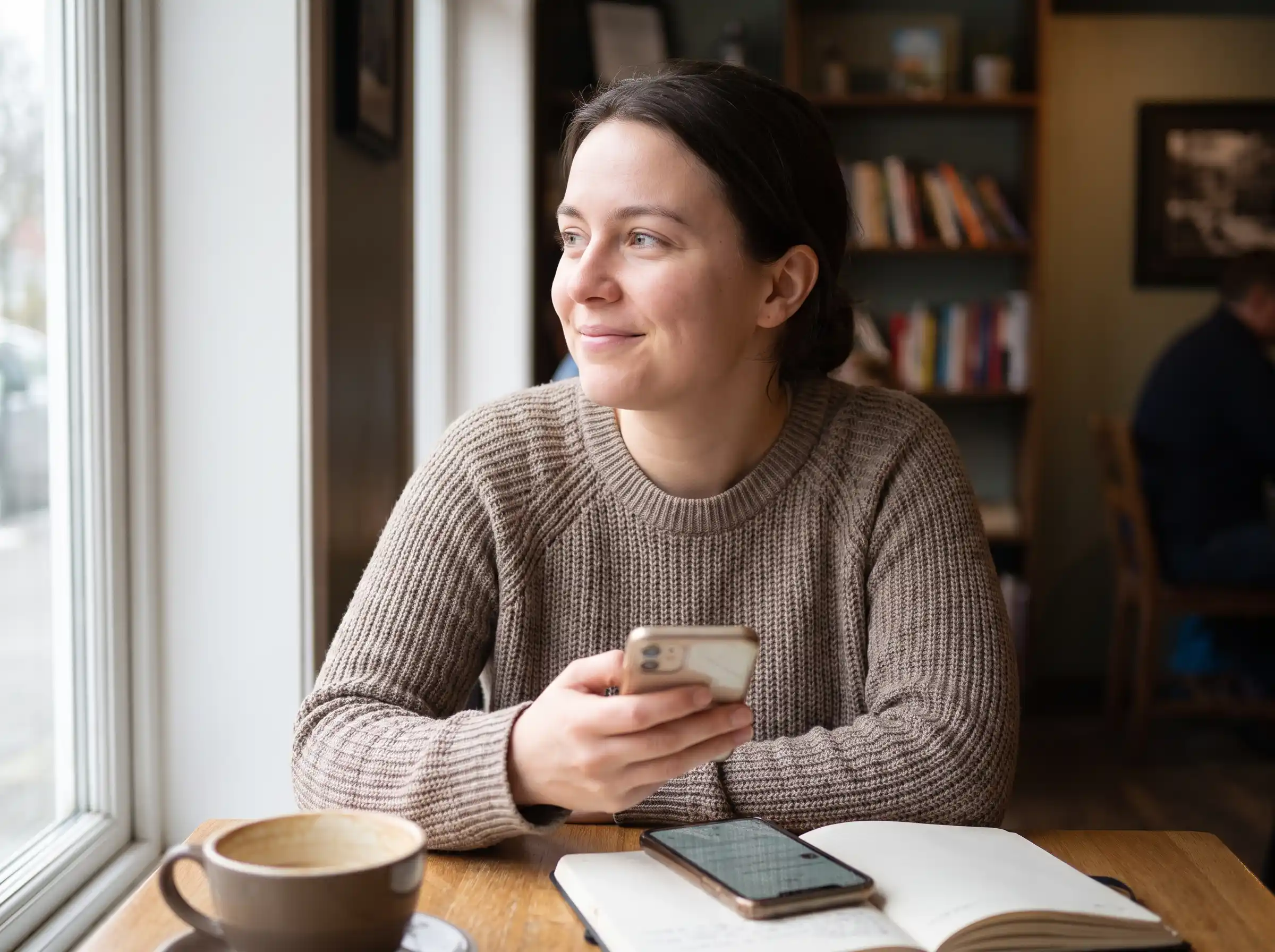 Woman relaxing by a window smiling at her phone, representing a calmer, more personal way of following content on Kuaishou